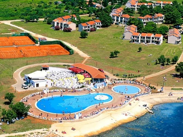 Here we can see water, swimming pools, people, and grass. There are vehicles on the road. Here we...