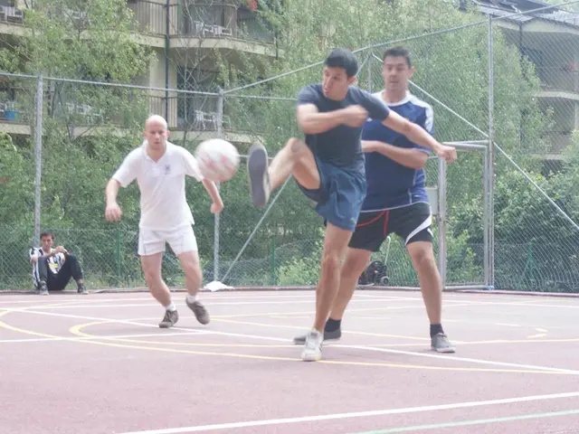 As we can see in the image there are few people here and there, ball, fence, trees and buildings.