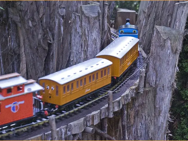 In this image we can see kids train which is moving on track in between the tree trunk and on right...
